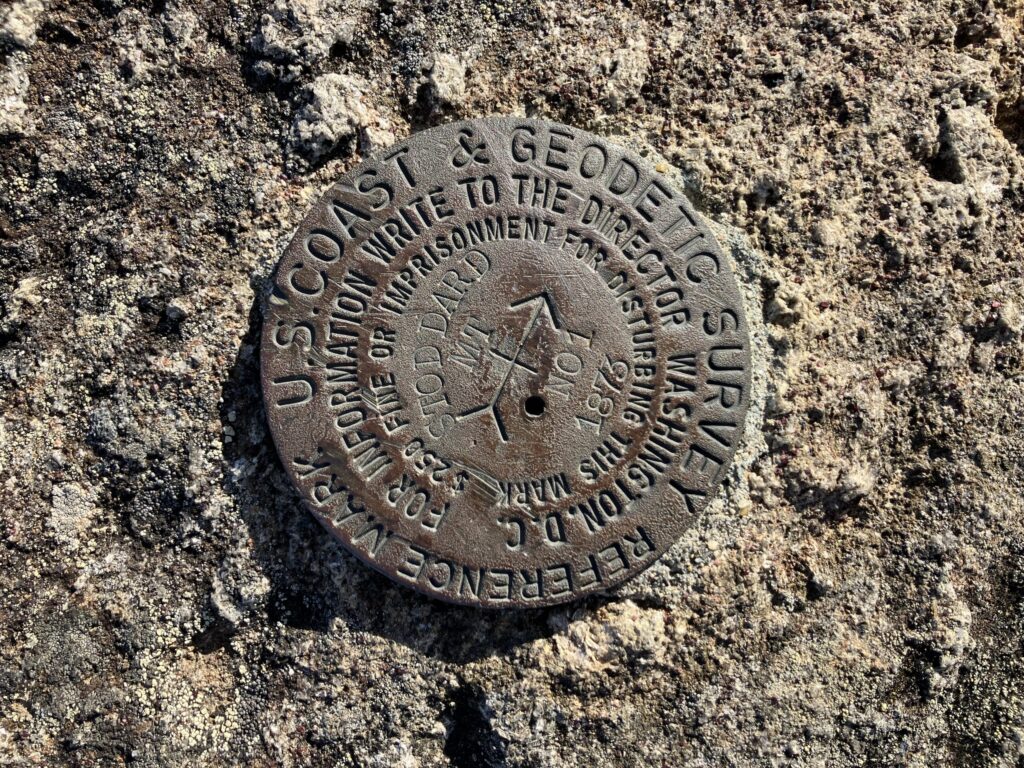 Closeup photograph of a U.S. Coast and Geodetic survey reference mark medallion sunk into rock. Standard benchmark text one finds stamped into such things except the words "Stoddard MT 1873" on either side of an arrow pointing to, presumably Stoddard Mountain.